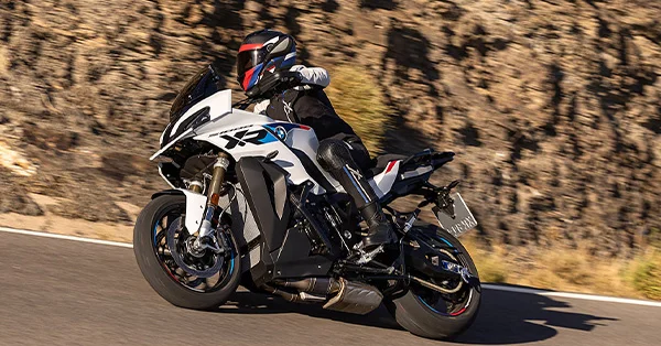 2026 BMW S 1000 XR sport-touring motorcycle on a mountain road, shown outdoors in a dynamic riding scene.